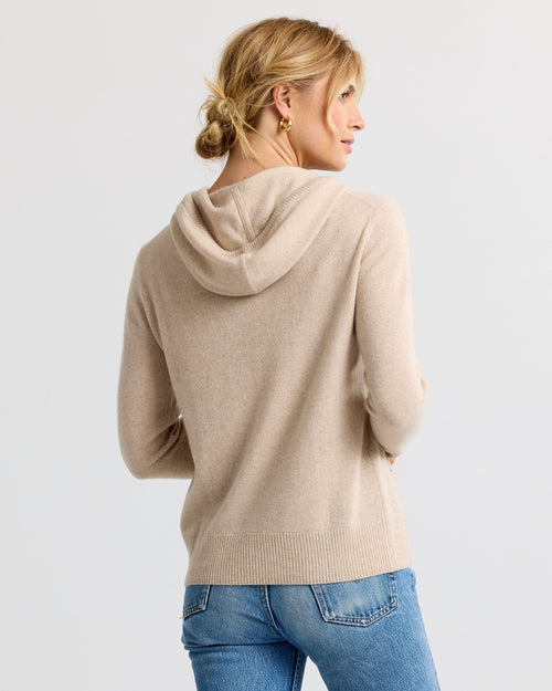 Woman wearing sand orange cashmere hoodie, back view, paired with blue jeans against plain background
