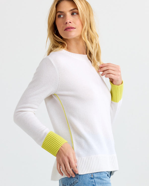 LIFESTYLE / EDITORIAL: Woman wearing white cashmere sweater with citron yellow cuffs and side seam detail, posing sideways