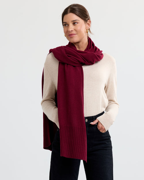 LIFESTYLE / EDITORIAL: Woman wearing beige cashmere sweater and barolo red cashmere scarf with black pants against white