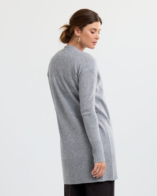LIFESTYLE / EDITORIAL: Woman wearing long grey cashmere sweater, standing sideways against plain white background
