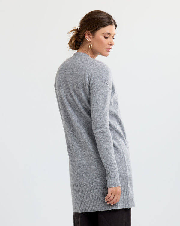 LIFESTYLE / EDITORIAL: Woman wearing long grey cashmere sweater, standing sideways against plain white background