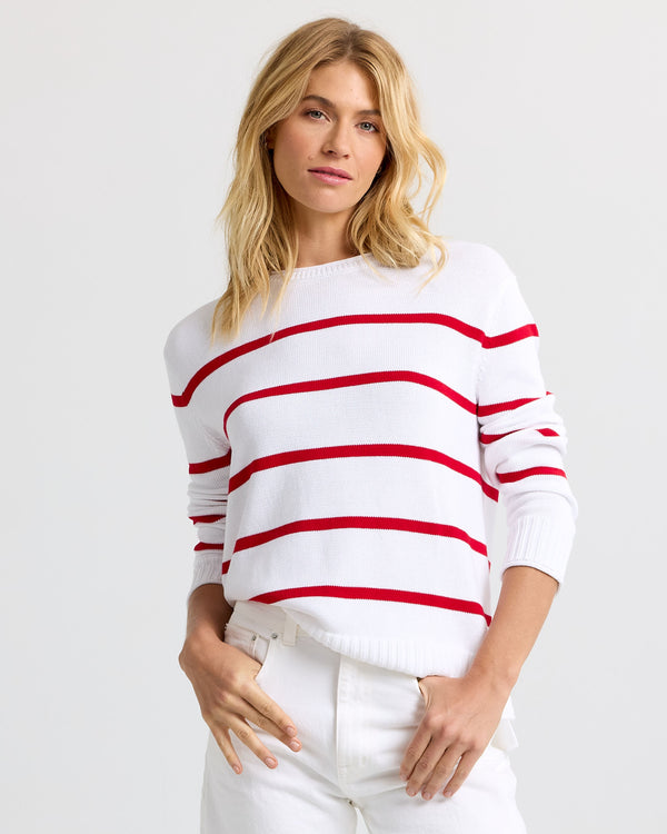LIFESTYLE / EDITORIAL: Woman wearing white sweater with red horizontal stripes and white pants against plain background