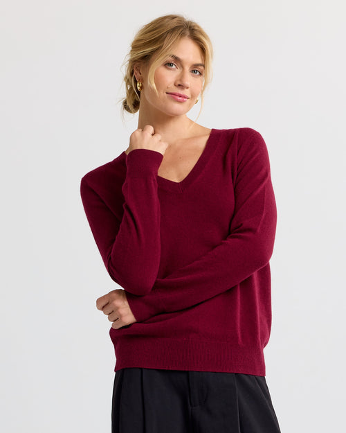 LIFESTYLE / EDITORIAL: Woman wearing a barolo red V-neck cashmere sweater with black pants, standing against a white