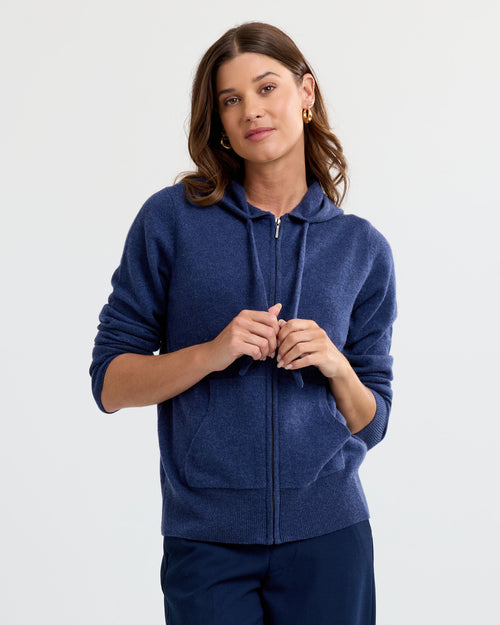 LIFESTYLE / EDITORIAL: Woman wearing indigo zip-up cashmere hoodie and navy pants against plain background