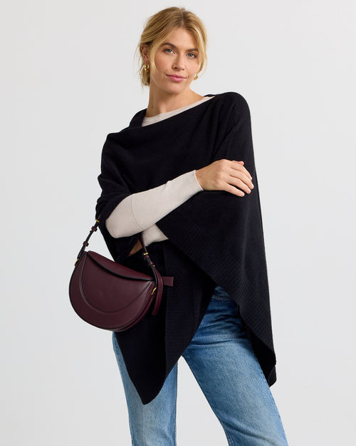 LIFESTYLE / EDITORIAL: Woman wearing black cashmere poncho, beige sweater, blue jeans, holding burgundy handbag against