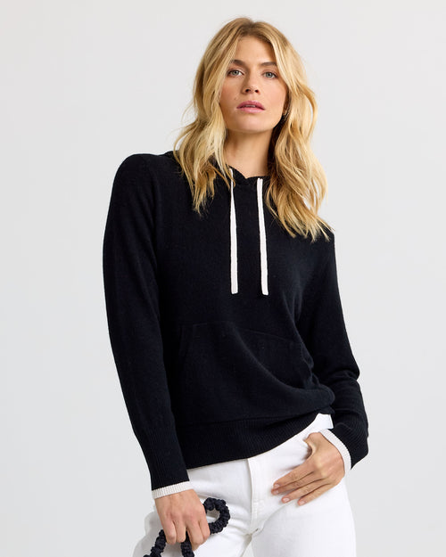 LIFESTYLE / EDITORIAL: Woman wearing black cashmere hoodie with white drawstrings and white pants against plain background