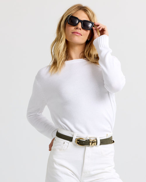 LIFESTYLE / EDITORIAL: Woman wearing white cashmere sweater and pants with black sunglasses and green belt against white