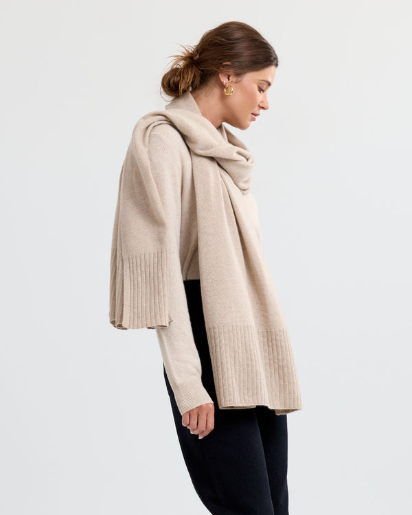 LIFESTYLE / EDITORIAL: Woman wearing beige cashmere sweater and scarf, standing in profile against plain background