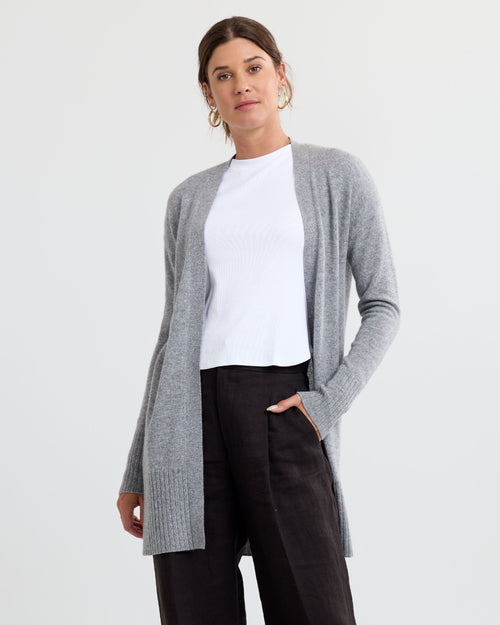 LIFESTYLE / EDITORIAL: Woman wearing gray open-front cashmere cardigan, white top, and black pants against plain background