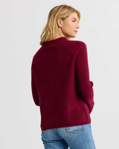 LIFESTYLE / EDITORIAL: Woman in barolo red ribbed cashmere sweater and light blue jeans, facing sideways against white