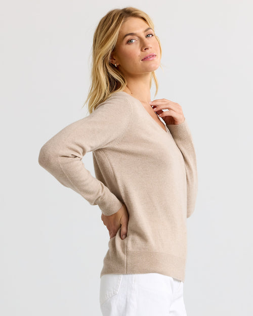 LIFESTYLE / EDITORIAL: Woman wearing beige cashmere sweater and white pants, posing against plain light background