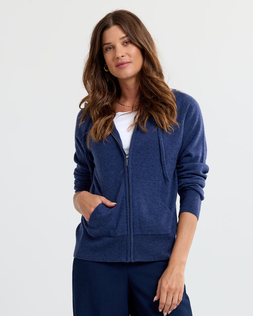 Front view image of a woman wearing an indigo zip-up cashmere hoodie and navy pants with hand in pocket
