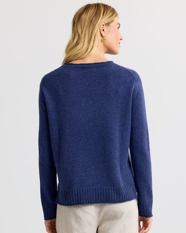 LIFESTYLE / EDITORIAL: Woman wearing indigo cashmere sweater, back view, with beige pants against a plain background