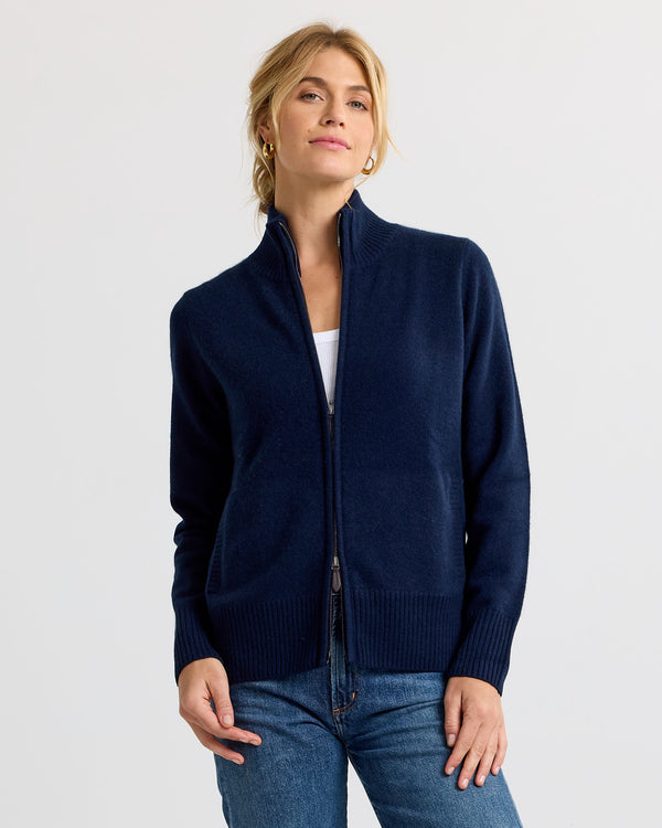LIFESTYLE / EDITORIAL: Woman wearing navy zip-up cashmere sweater and jeans against plain white background