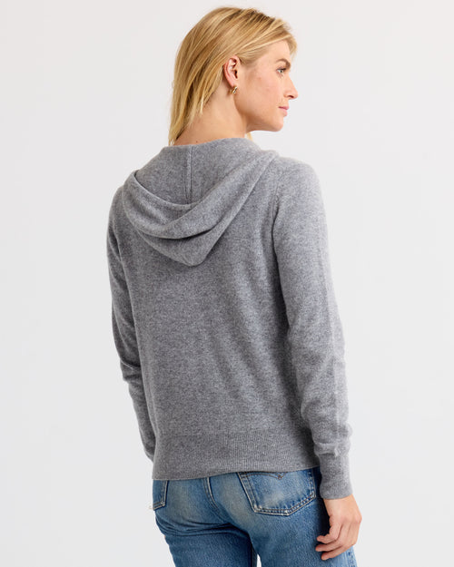 Woman wearing light gray cashmere hoodie sweater, shown from back, paired with blue jeans against white background