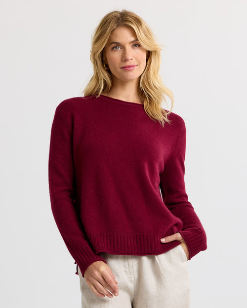 LIFESTYLE / EDITORIAL: Woman wearing a barolo-colored cashmere sweater with cream pants against a plain background