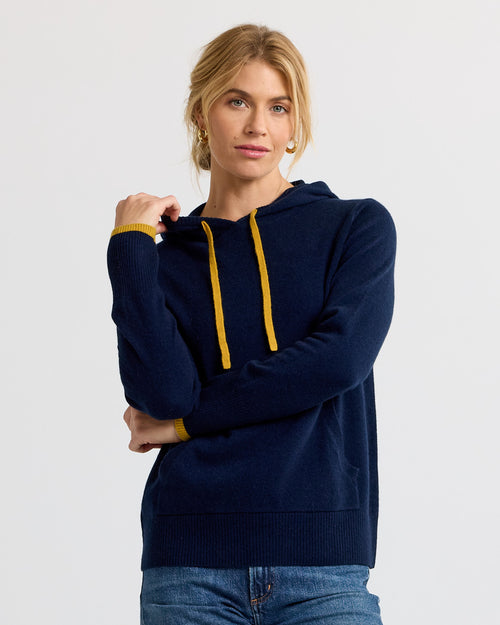 Woman wearing navy blue cashmere hoodie with yellow drawstrings and cuffs, standing against plain white background