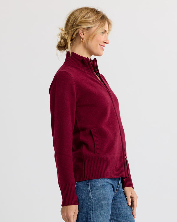 LIFESTYLE / EDITORIAL: Woman in burgundy zip-up cashmere sweater and blue jeans, side profile against white background