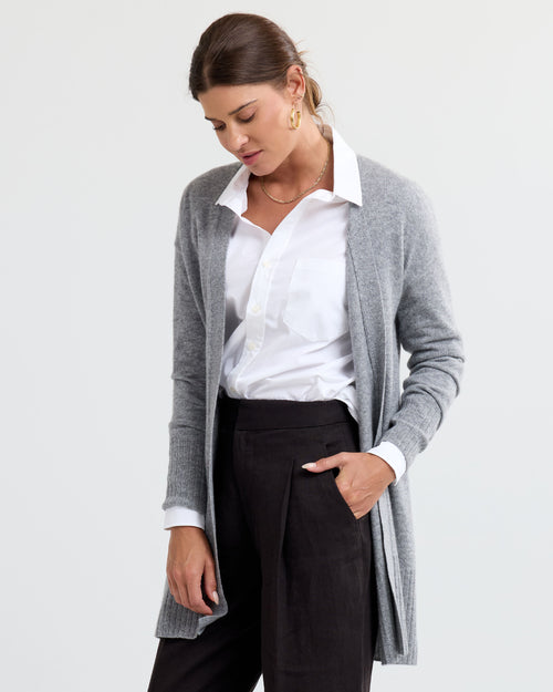LIFESTYLE / EDITORIAL: Woman wearing gray cashmere cardigan over white shirt and black pants, standing against white