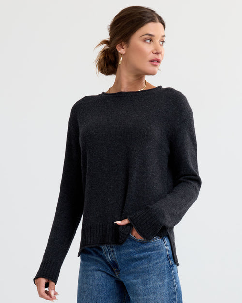 Three-quarter view image of a woman wearing a charcoal cashmere sweater and blue jeans, looking to her left