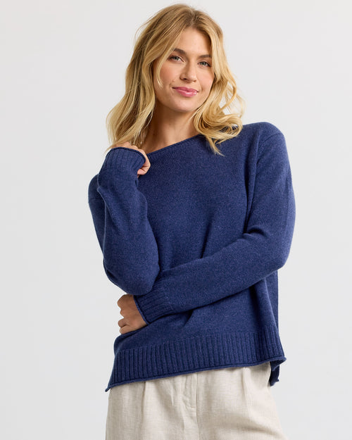 LIFESTYLE / EDITORIAL: Woman wearing indigo blue cashmere sweater with beige pants against white background