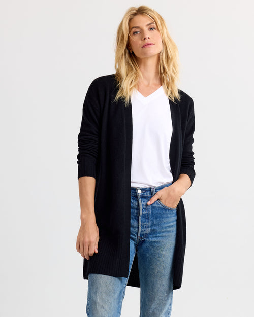 LIFESTYLE / EDITORIAL: Woman wearing black long cashmere cardigan, white V-neck shirt, and blue jeans against white
