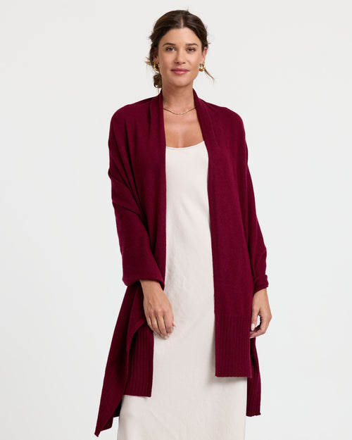 LIFESTYLE / EDITORIAL: Woman wearing a long burgundy cashmere cardigan over a white dress, standing against a white