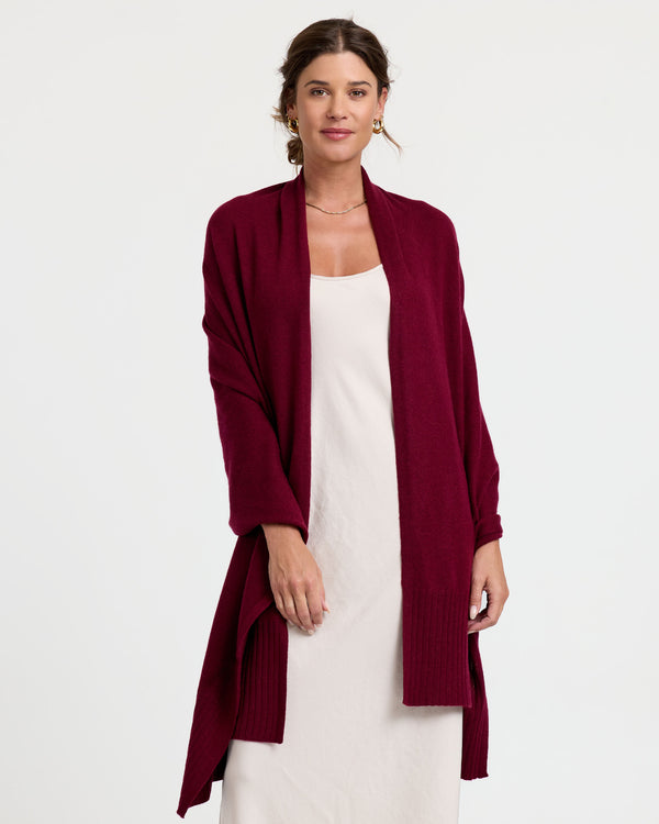 LIFESTYLE / EDITORIAL: Woman wearing a long burgundy cashmere cardigan over a white dress, standing against a white