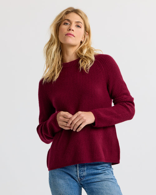 LIFESTYLE / EDITORIAL: Woman wearing a burgundy ribbed cashmere sweater and blue jeans against a plain background