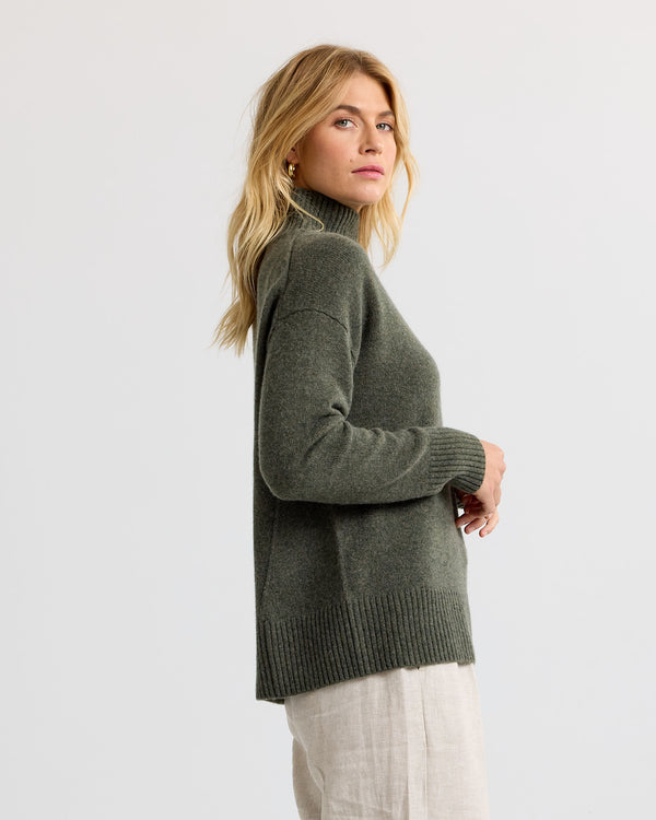 Dark olive cashmere funnel neck sweater with light trousers, side view