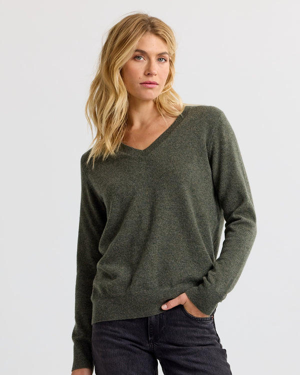 Front three-quarter image of a woman wearing a dark olive V-neck cashmere sweater with black jeans standing