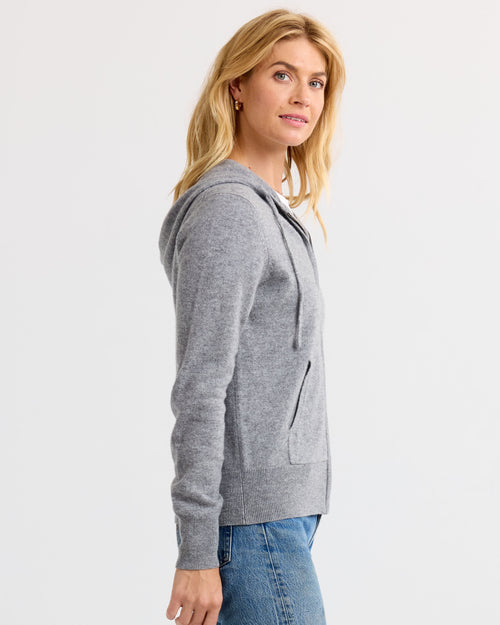 LIFESTYLE / EDITORIAL: Woman wearing grey cashmere hoodie and blue jeans, standing sideways against white background