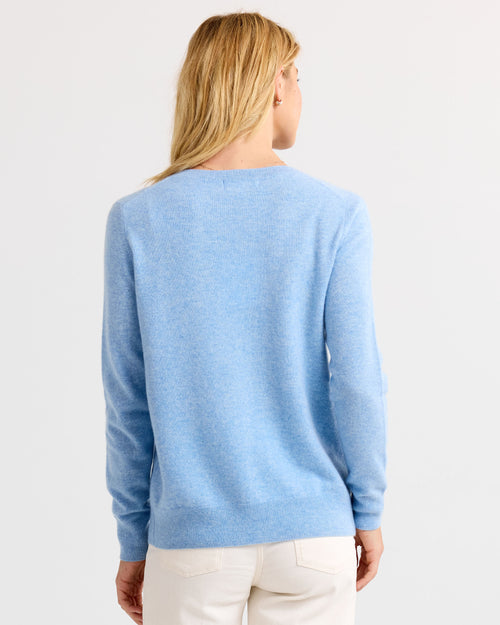 Woman wearing light blue cashmere sweater and white pants, back view, plain background