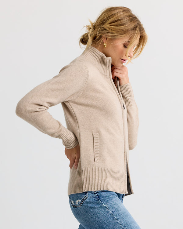 LIFESTYLE / EDITORIAL: Woman in beige zip-up cashmere sweater and blue jeans, side profile against plain background