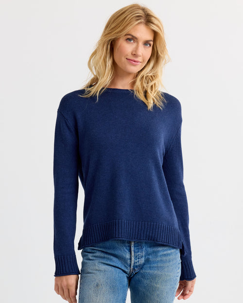 LIFESTYLE / EDITORIAL: Woman wearing navy blue cashmere sweater and blue jeans against white background