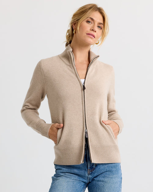 LIFESTYLE / EDITORIAL: Woman wearing a cappuccino-colored zip-up cashmere sweater with hands in pockets and blue jeans