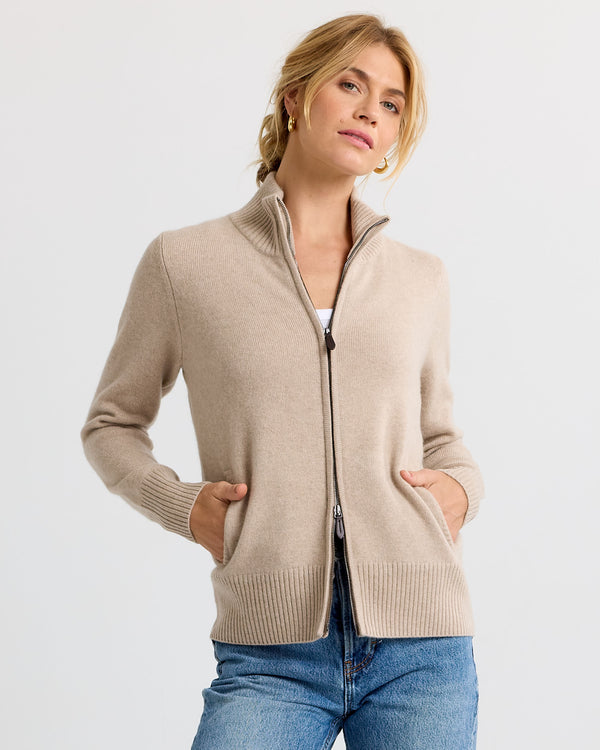 LIFESTYLE / EDITORIAL: Woman wearing a cappuccino-colored zip-up cashmere sweater with hands in pockets and blue jeans