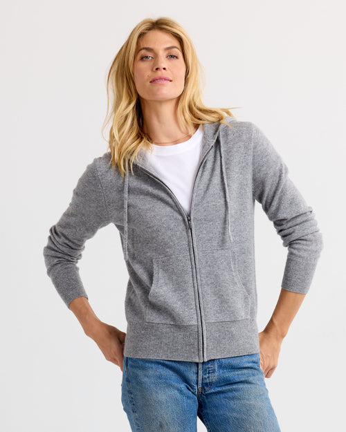 Front view image of a woman wearing grey zip-up cashmere hoodie with pockets over white tee and blue jeans