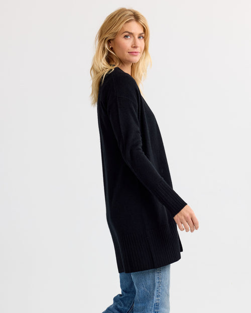 LIFESTYLE / EDITORIAL: Woman wearing long black cashmere cardigan and blue jeans, standing sideways against white background