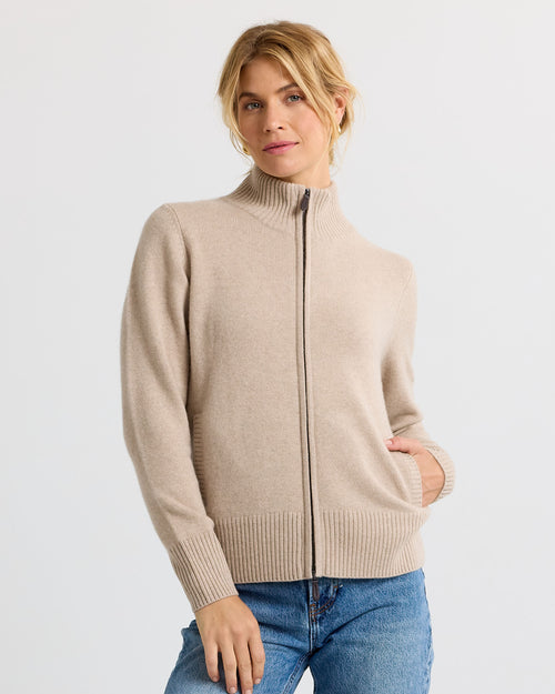 Woman wearing beige zip-up cashmere sweater and blue jeans against white background