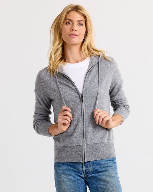 Front view image of a woman wearing a grey zip-up cashmere hoodie with a white tee and blue jeans