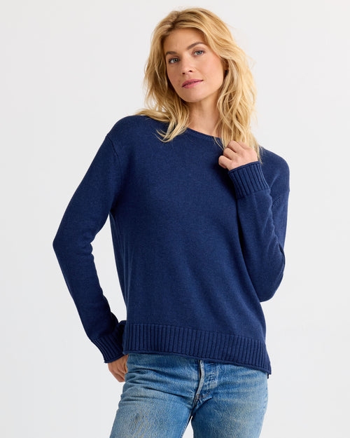 Three-quarter image of a woman wearing a navy blue cashmere sweater and jeans with hand near the neck