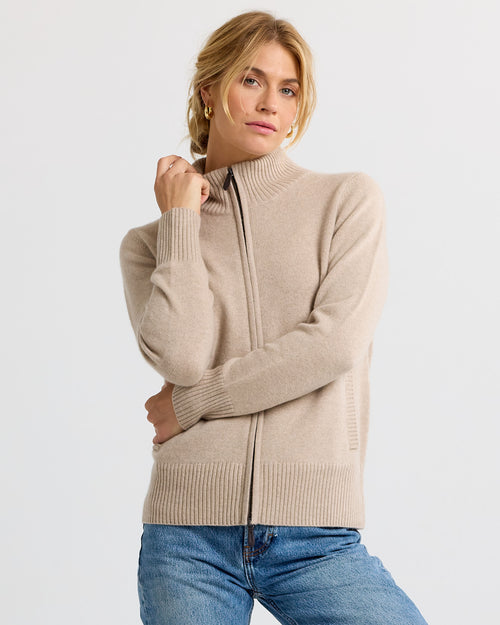 LIFESTYLE / EDITORIAL: Woman wearing cappuccino color zip-up cashmere sweater and blue jeans against plain background