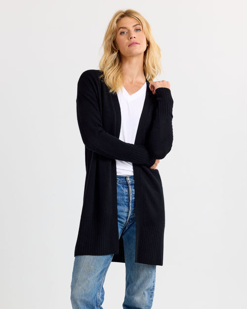 LIFESTYLE / EDITORIAL: Woman wearing black open-front cashmere cardigan over white shirt and blue jeans against white