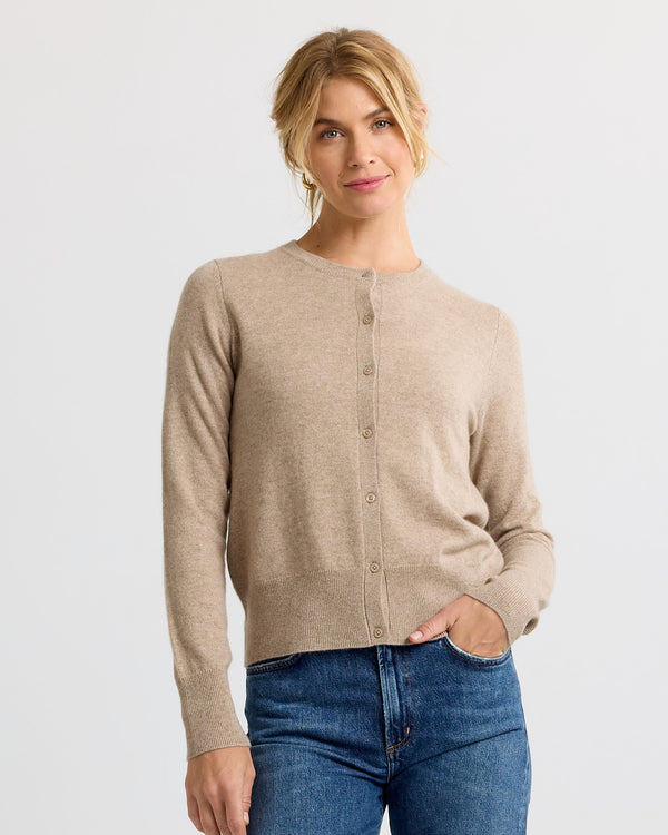 LIFESTYLE / EDITORIAL: Woman wearing beige cashmere cardigan and blue jeans against plain white background