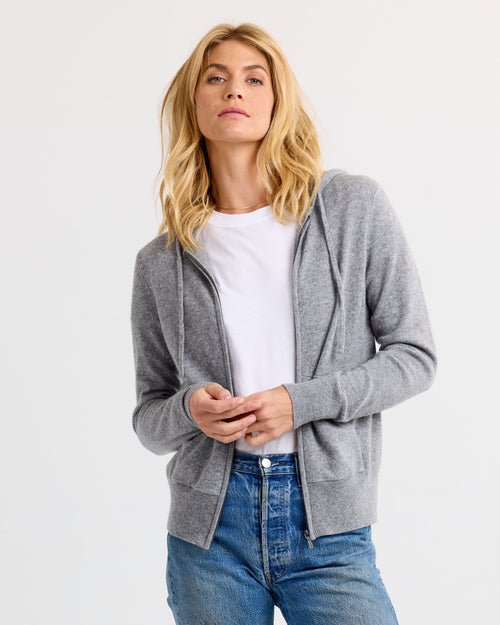 Front view image of a woman wearing a grey cashmere zip-up hoodie over a white t-shirt and blue jeans.