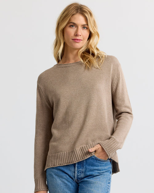Front three-quarter image of a woman wearing a taupe cashmere sweater and blue jeans against a plain background