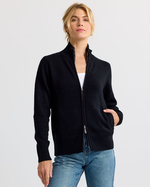 Front view image of a woman wearing a black zip-up cashmere sweater with hands in pockets and blue jeans