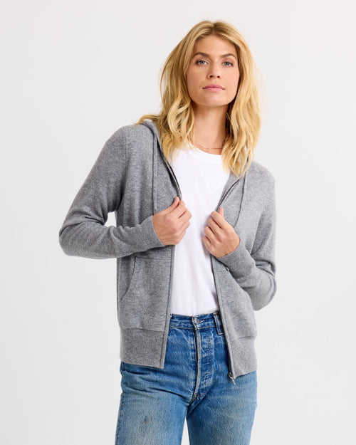 LIFESTYLE / EDITORIAL: Woman wearing grey zip-up cashmere hoodie over white tee and blue jeans against white background