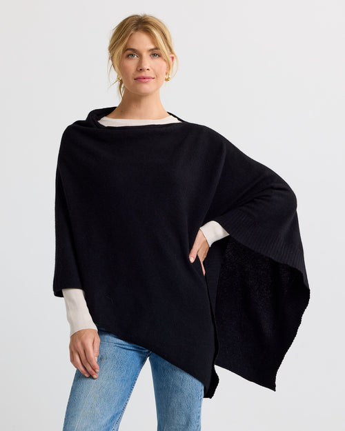 LIFESTYLE / EDITORIAL: Woman wearing black cashmere poncho with asymmetrical hem and light sweater underneath, blue jeans